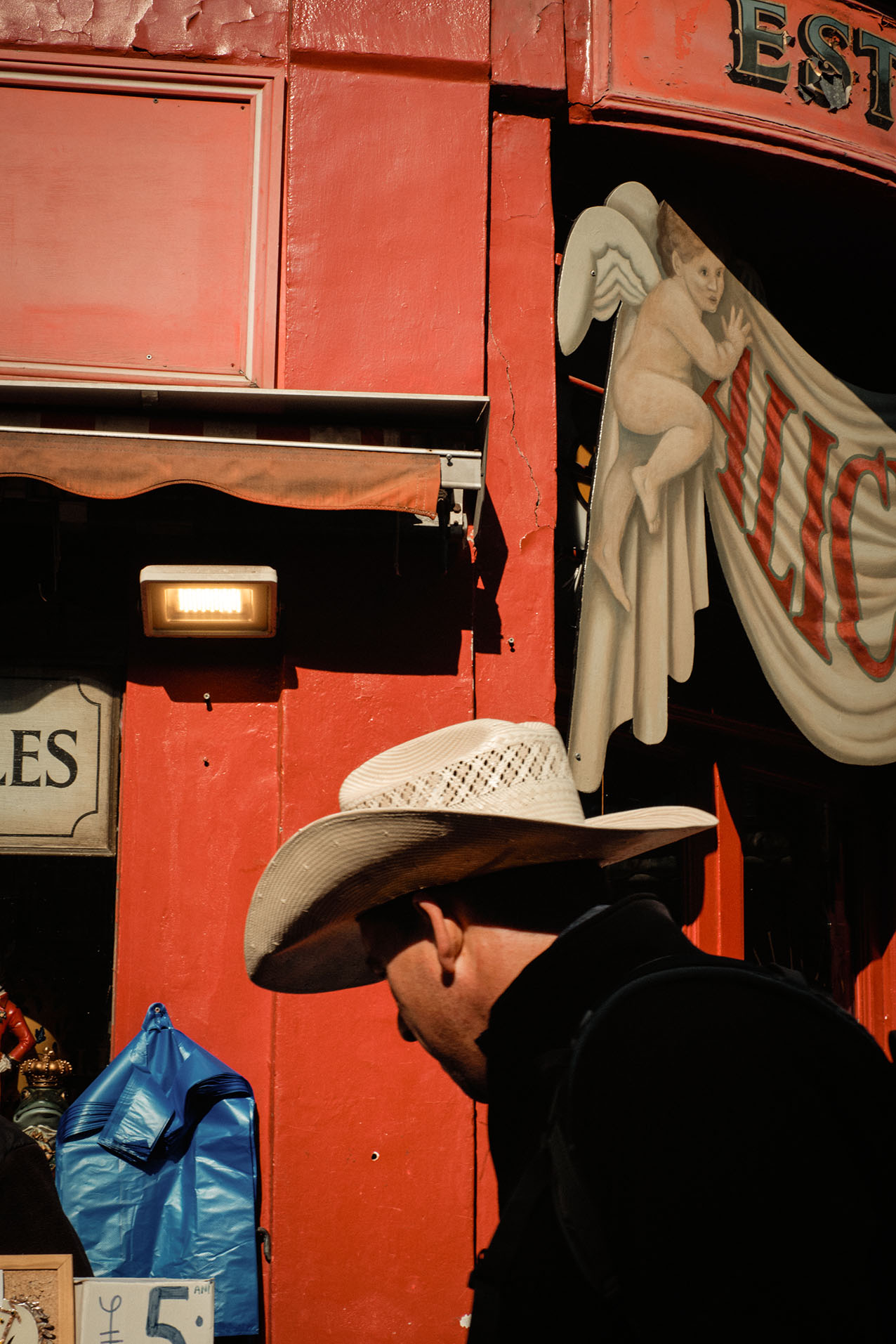 A man on the phone walks towards a car outside a neon-lit club sign reading Tables & Dancing at night