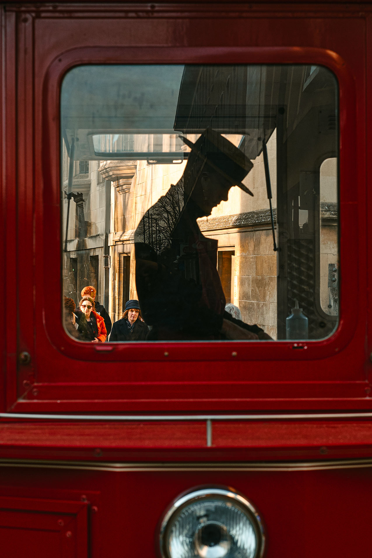 A man in a blue jumper sits at a cafe table outside a window, framed by blurred signage