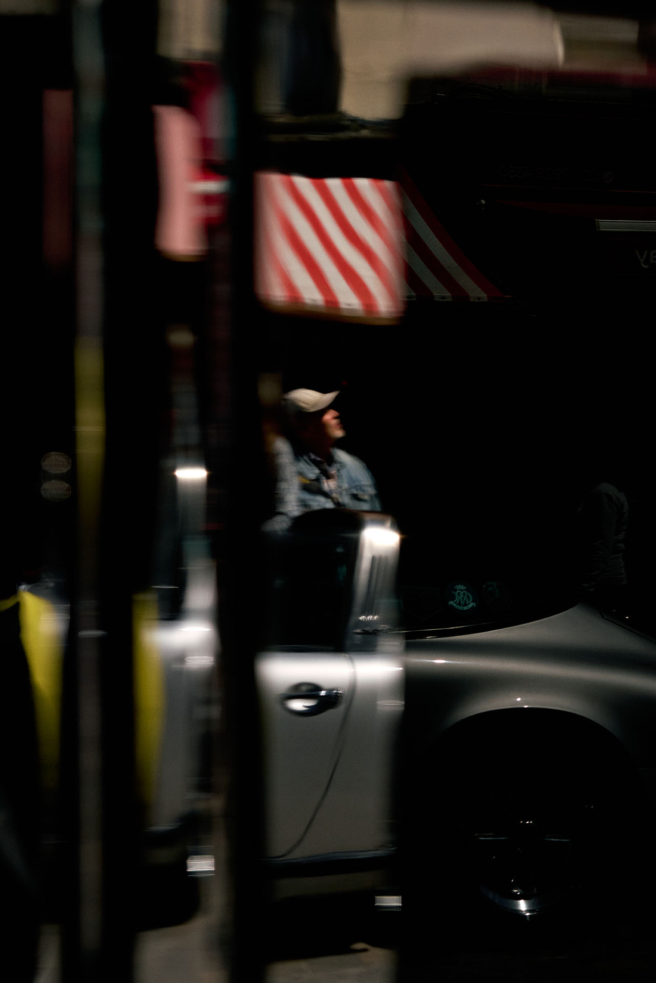 A man on the phone walks towards a car outside a neon-lit club sign reading Tables & Dancing at night