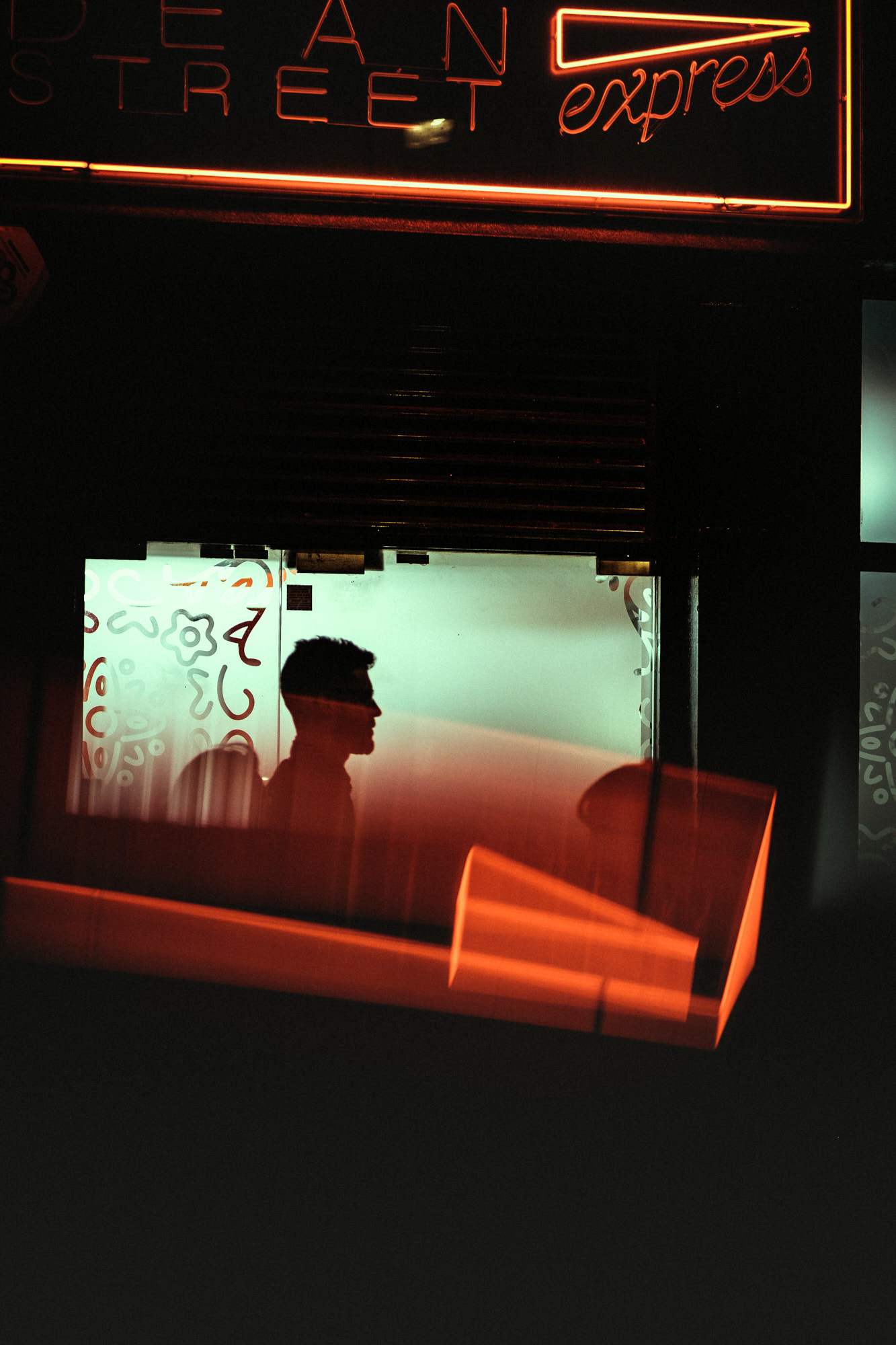 A man on the phone walks towards a car outside a neon-lit club sign reading Tables & Dancing at night