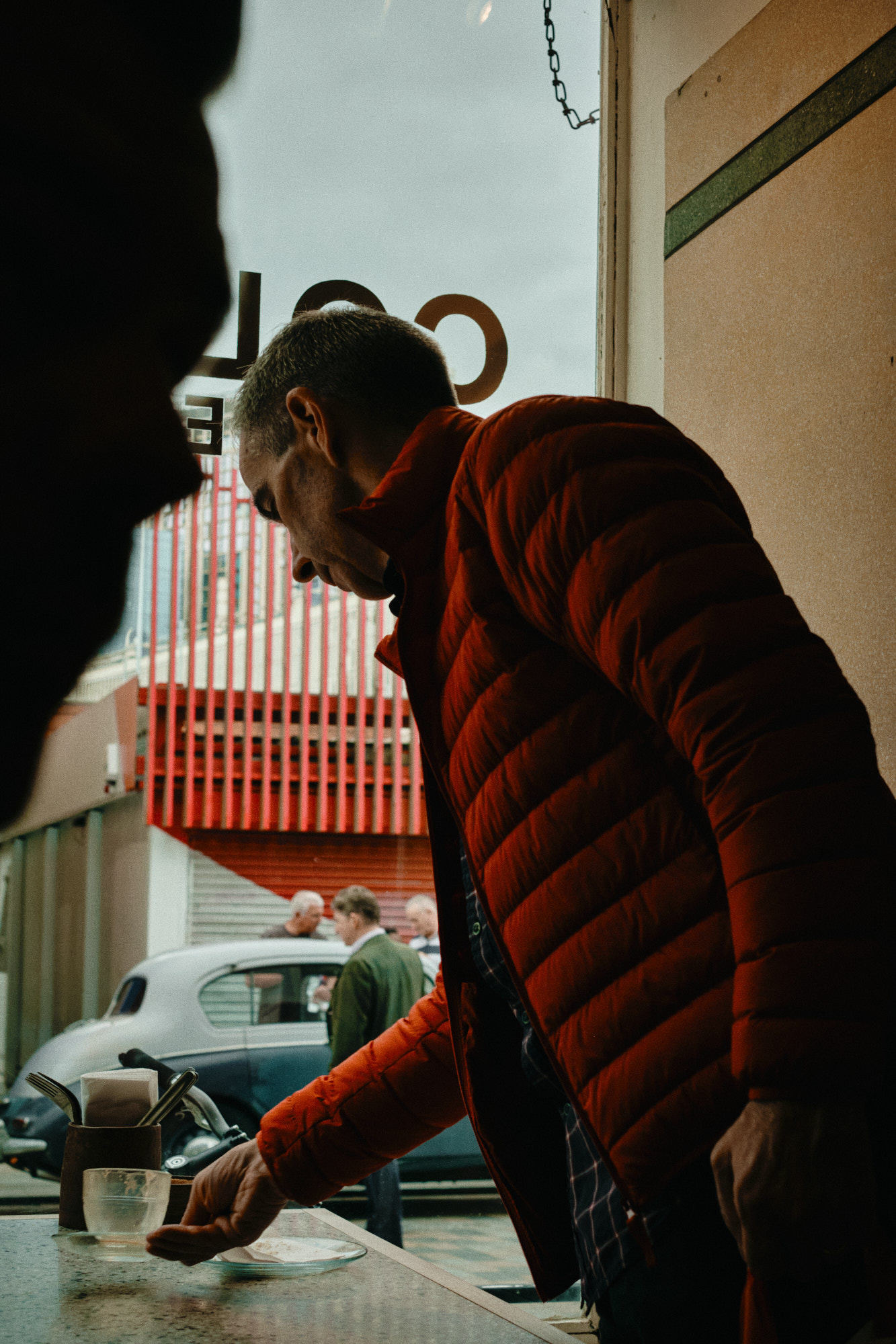A man on the phone walks towards a car outside a neon-lit club sign reading Tables & Dancing at night
