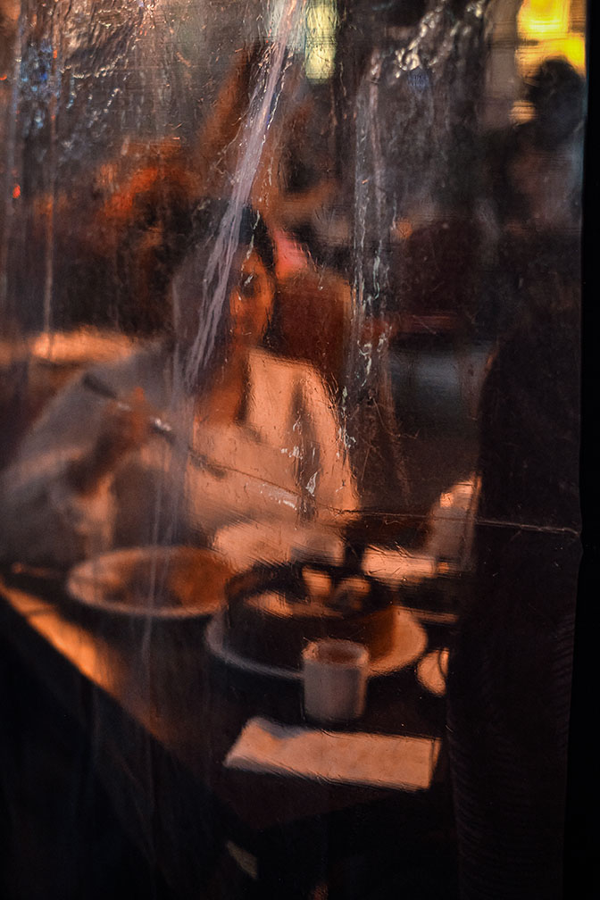 A man on the phone walks towards a car outside a neon-lit club sign reading Tables & Dancing at night