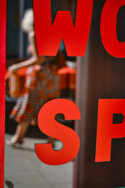 A man on the phone walks towards a car outside a neon-lit club sign reading Tables & Dancing at night