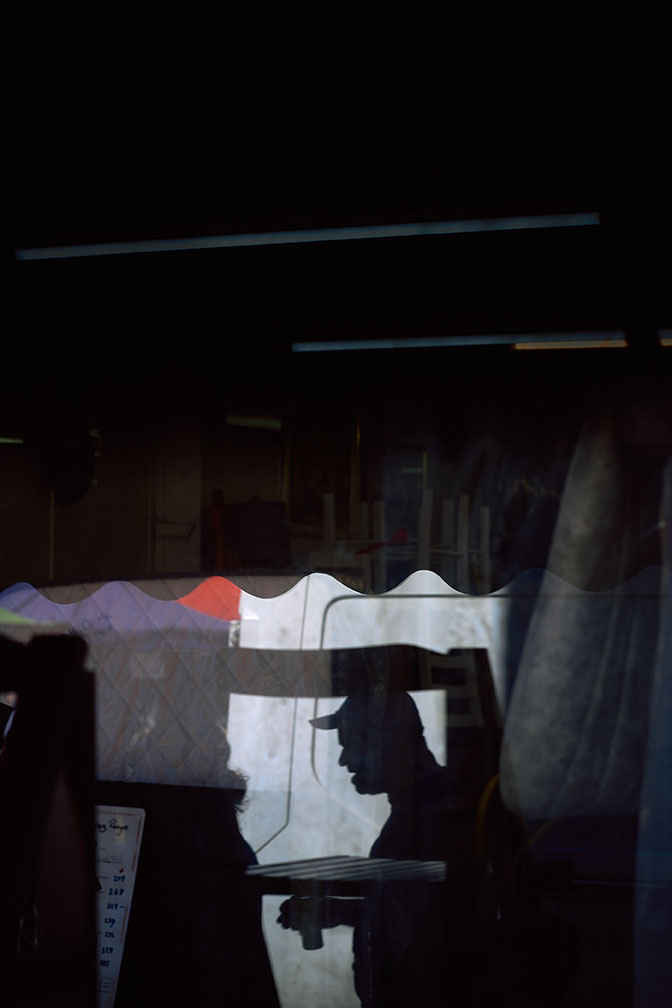 A man on the phone walks towards a car outside a neon-lit club sign reading Tables & Dancing at night