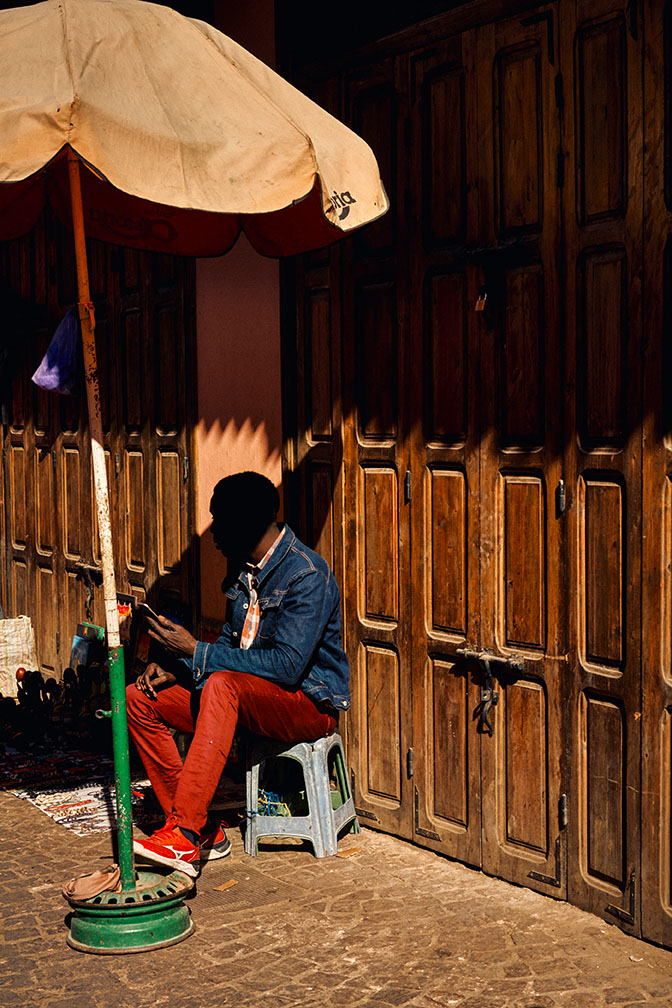 A man on the phone walks towards a car outside a neon-lit club sign reading Tables & Dancing at night